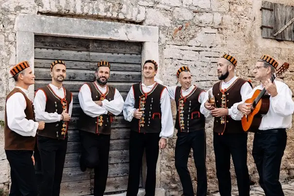 Na slici su članovi dalmatinske klape Bunari, poznate vokalne skupine koja izvodi tradicionalne dalmatinske pjesme a cappella, često uz pratnju gitare ili mandoline. Klape poput Bunara nezaobilazan su dio dalmatinske kulturne baštine i često nastupaju na raznim događajima. Oliver Jakovčev poznat je po pjesmi "Betinska balada" koja slavi ljepote Betine.