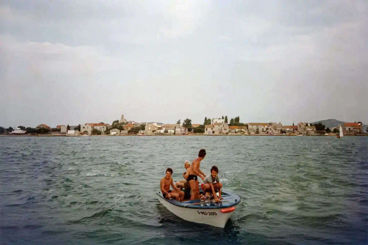 Slika prikazuje mali čamac po imenu Tonči, koji je vozio dida, unuke i turiste ispred kuće gdje se danas nalaze apartmani An-Mar. Tonči je bio važan dio svakodnevnog života obitelji – simbol povezanosti s morem i zajedničkih trenutaka provedenih na moru, koje i danas čuvaju uspomene, tradiciju, ali i pouku. Jer, kako je dide uvijek govorio: „Fali more, drž se kraja!“