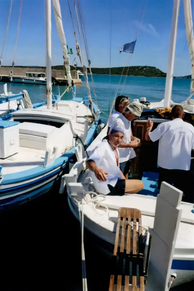 Slika prikazuje domaćina na Betinskoj gajeti — tradicionalnoj drvenoj jedrilici karakterističnoj za mjesto Betina na otoku Murteru, poznatoj po svojoj izradi i pomorskoj tradiciji — prije početka regate. Gajete su stoljećima bile važan dio lokalnog pomorstva, korištene za ribolov i prijevoz, a danas se održavaju i kao simbol baštine kroz natjecanja i regate.