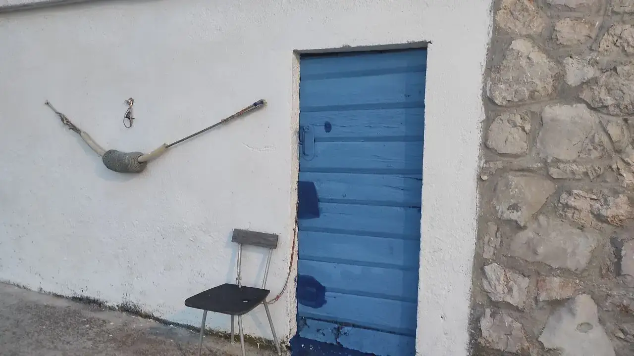 Naslovna 9 Slika prikazuje tradicionalnu kamenu ribarsku kućicu uz more na otoku Murteru, s karakterističnim drvenim vratima obojenima u dalmatinsku plavu boju. U ovakvim kućicama ribari su nekoć čuvali i mreže, parangale, vrše i ostali ribarski alat. Ispred kućice nalazi se jednostavna drvena stolica – mjesto za odmor i pletenje mreža s pogledom na more. Ova autentična scena odražava bogatu ribarsku tradiciju i spokojan ritam života uz more.